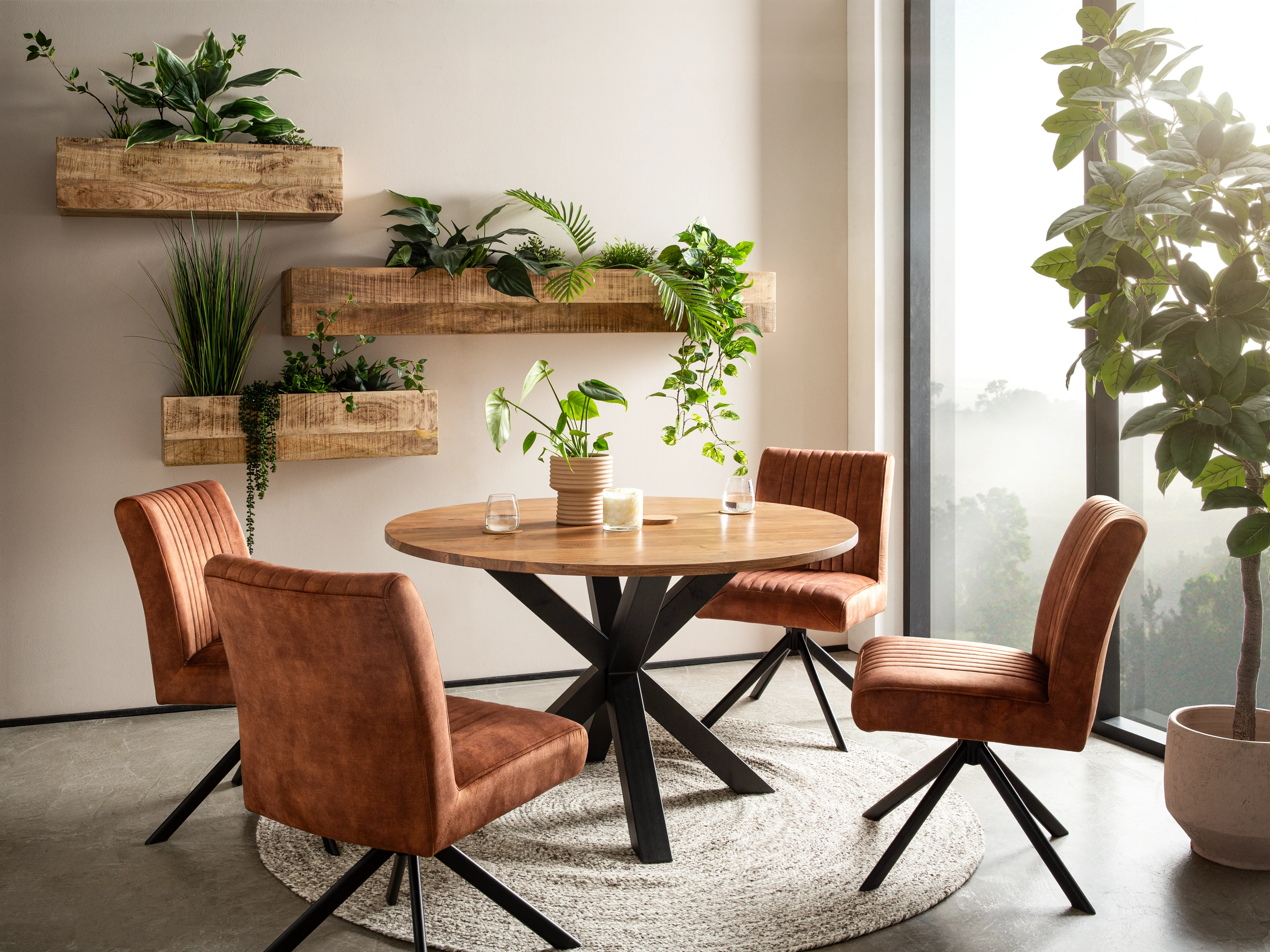 Wohnbeispiel: Essgruppe Cruzar, 45°-Ansicht eines runden Esstischs aus lackiertem Akazienholz mit vier Stühlen und Pflanzen.